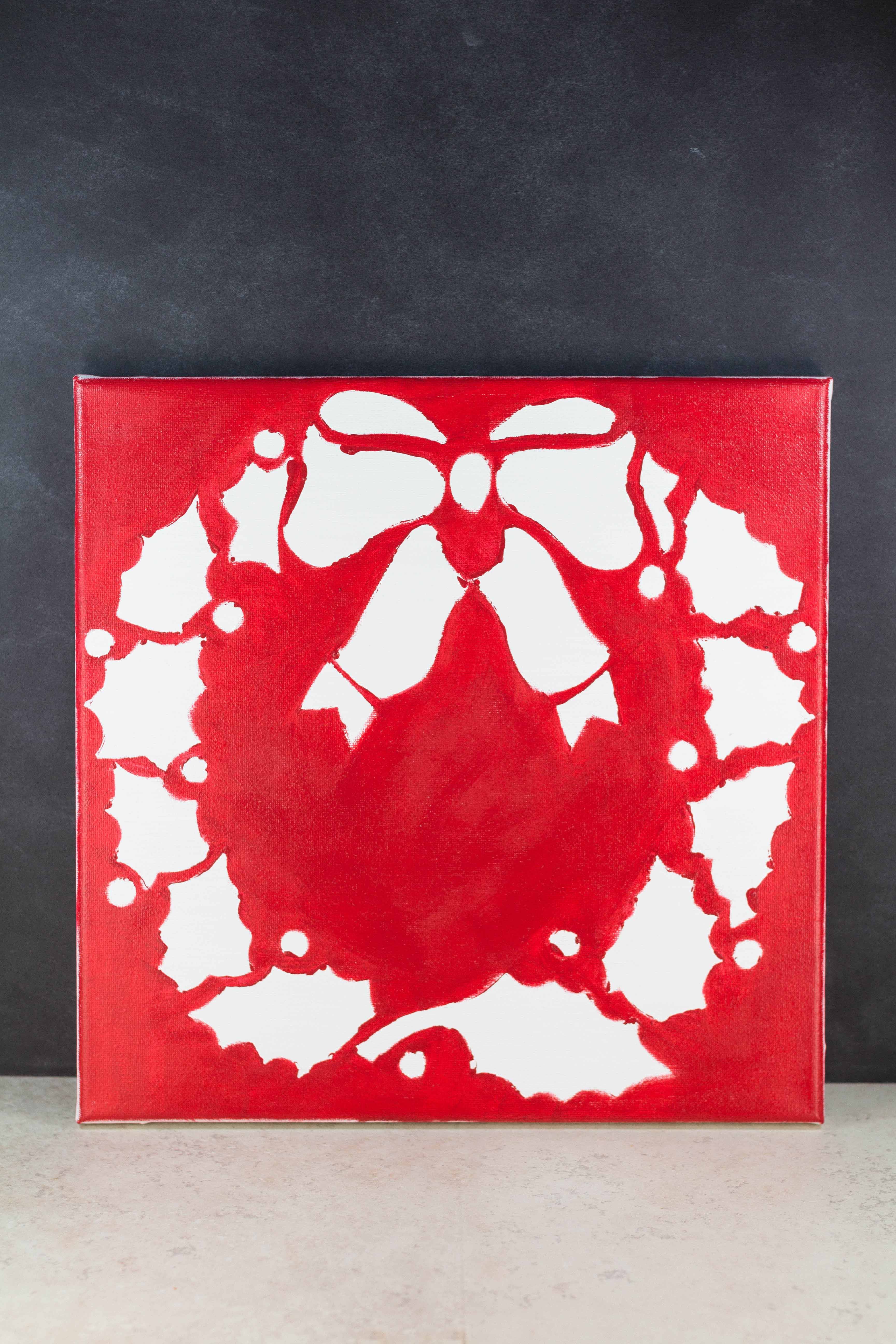 DIY Red Wreath Holiday Decor Canvas Wall Art, using a reverse stencil technique. Click through to learn how to make your own wreath art! | https://www.roseclearfield.com