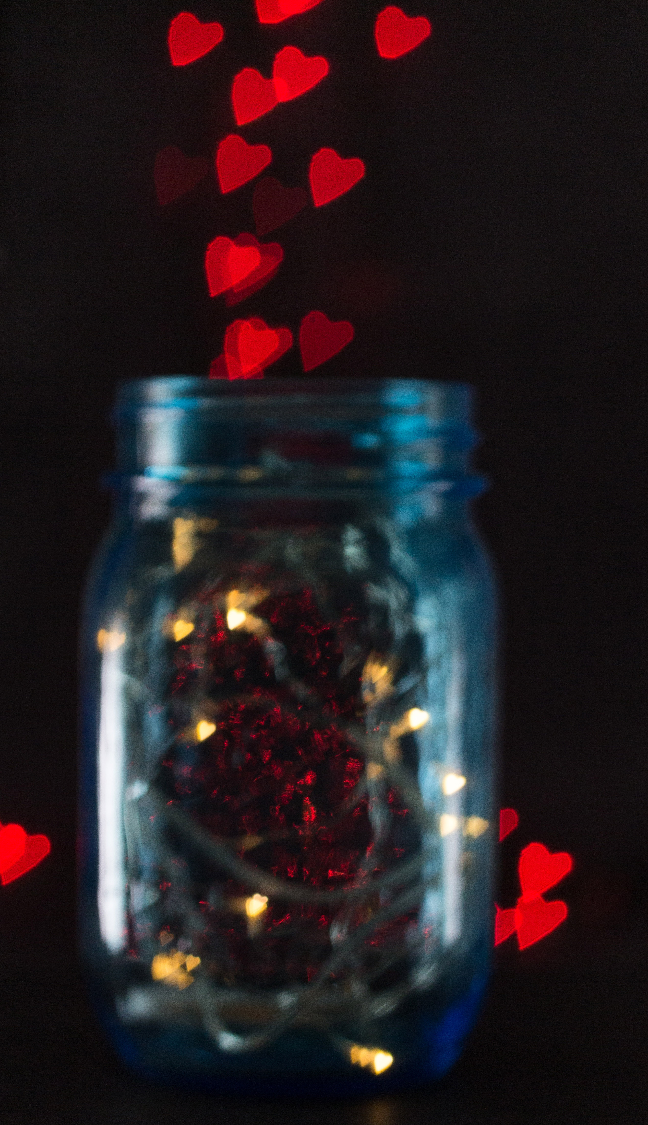 Blue mason jar with fairy lights and a red heart bokeh background. | https://www.roseclearfield.com