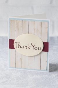 Simple DIY thank you card with a faux wood background and deep red strip behind a mounted oval "thank you." #thankyoucard #homemadecard #greetingcardinspiration | https://www.roseclearfield.com